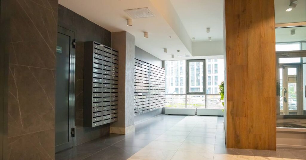 The lobby of a building where group mailbox compartments, mounted to the wall, are visible upon entering and exiting.