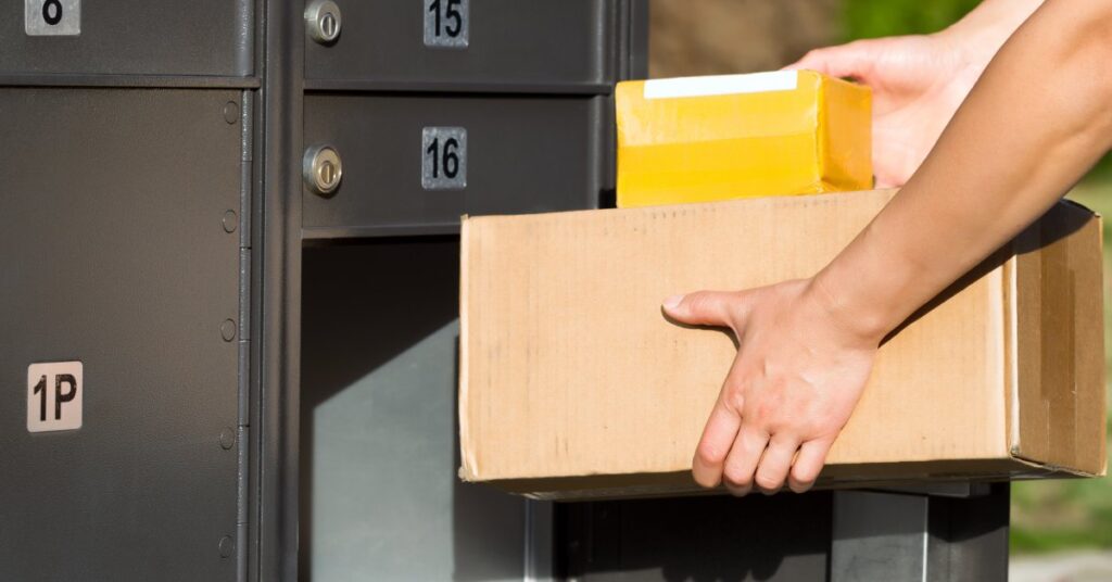 A closeup of a person's hands carrying two different sized boxes that are either going in or coming out of the mailbox.