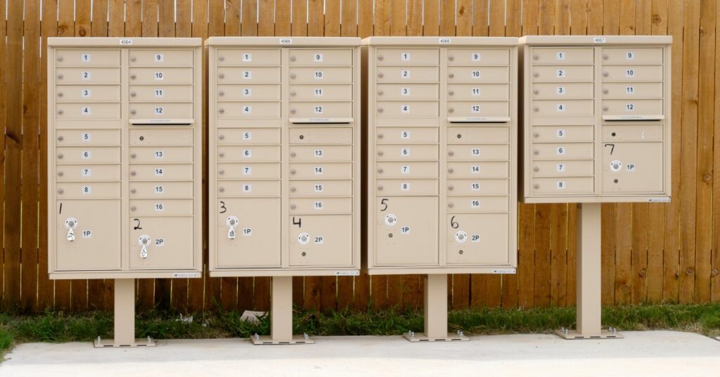 A row of lightly colored cluster mailbox units lined together with numbers one through seven written on them in ink.