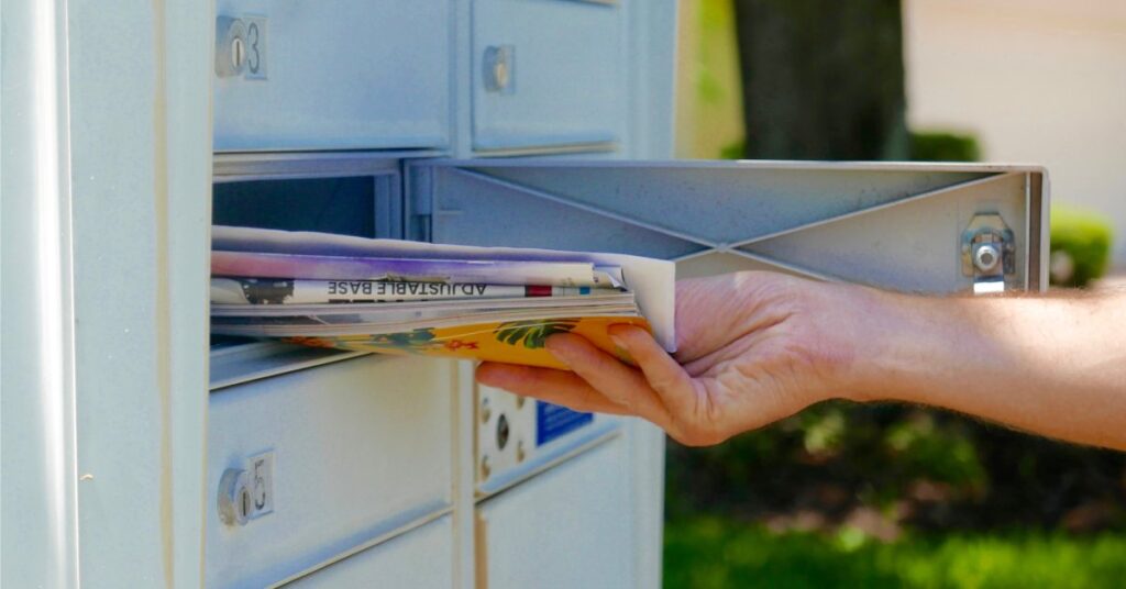 A closeup of a person's hand pulling a pile of mail out of an individual mail slot of a cluster mailbox.