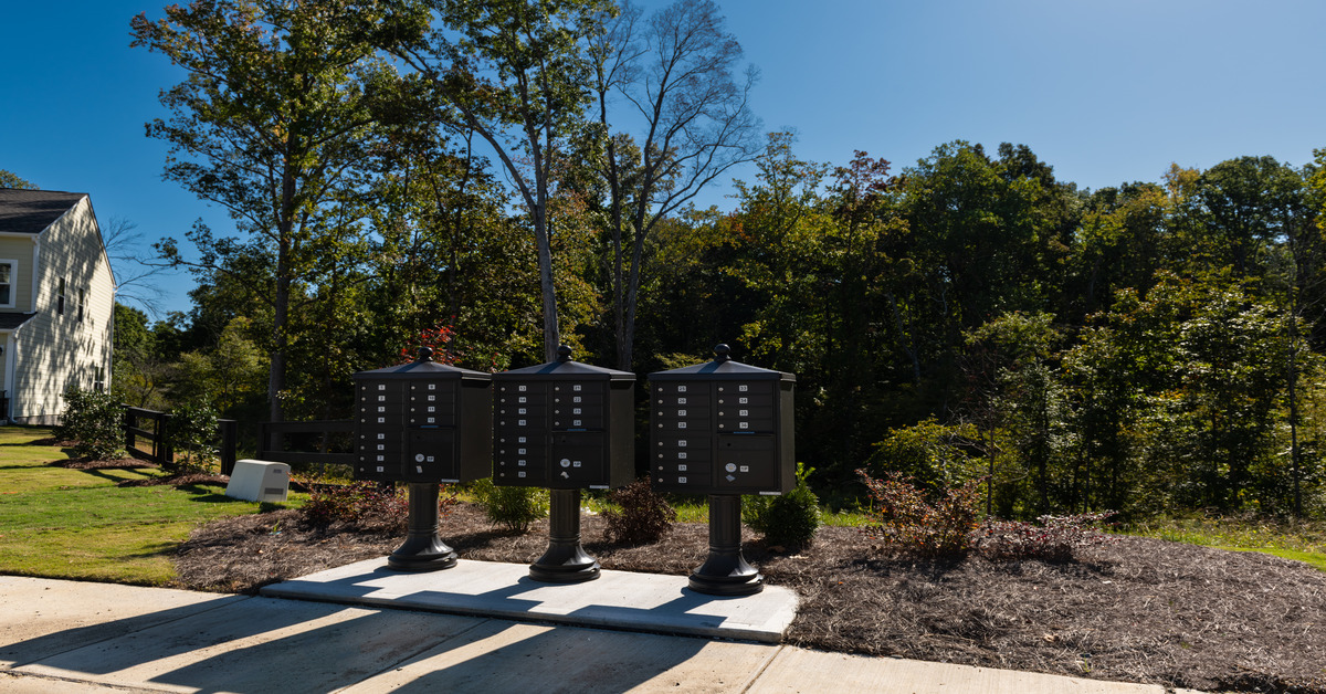 A row of three identical brown cluster mailboxes with pedestal designs positioned in front of trees and grass.