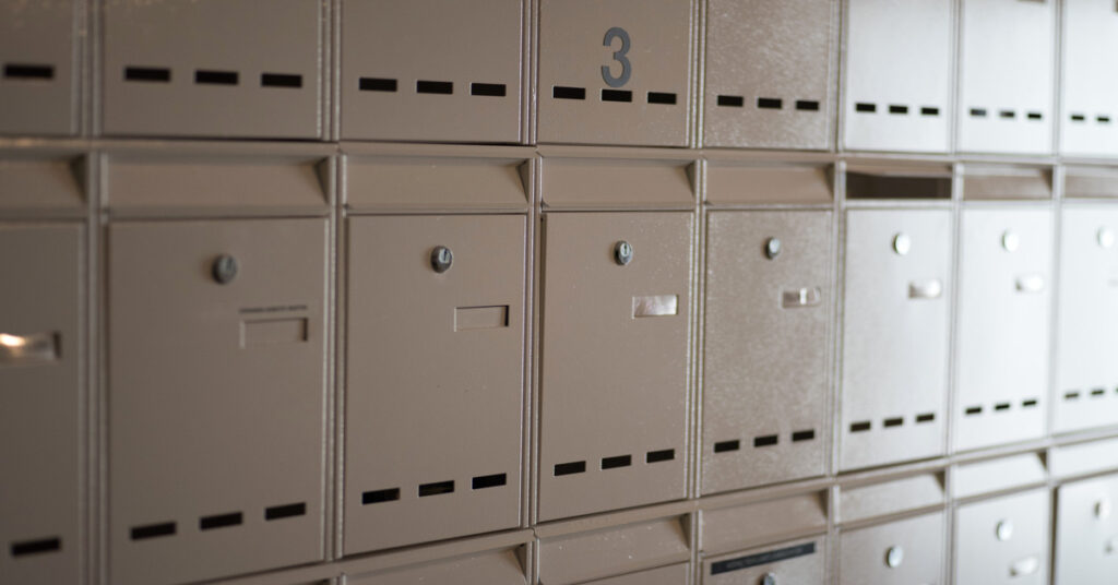 A black number "3" on a surface above a row of cluster mailbox units that are large enough for packages to fit into.