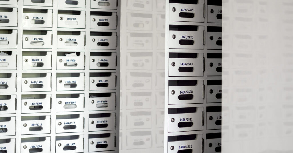 A secure mail room inside a building containing several white mailbox units with individual keyholes.
