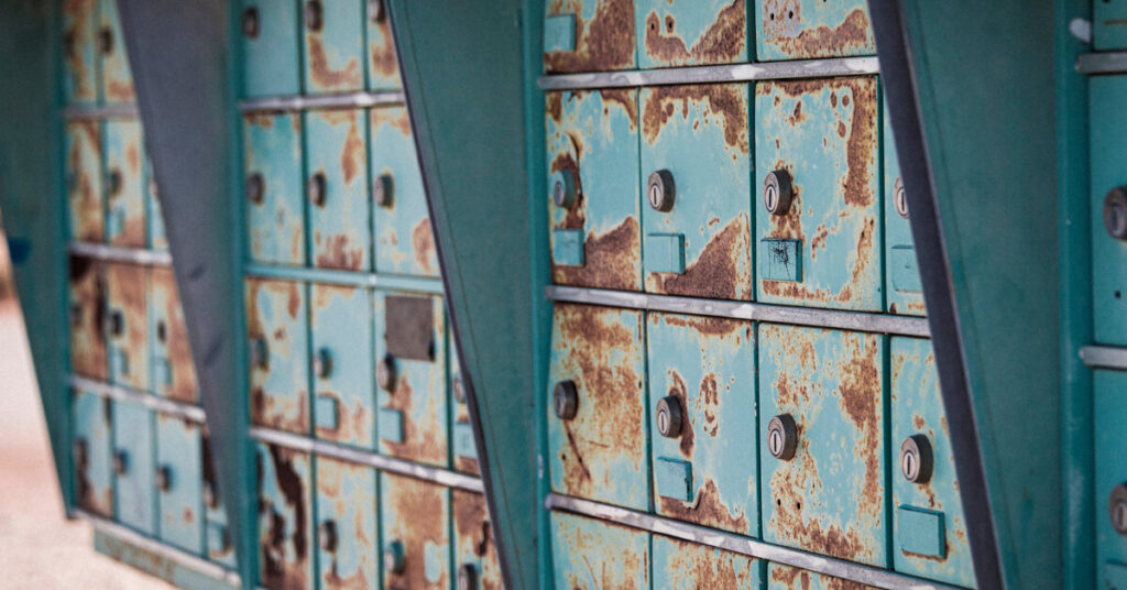 A cluster mailbox, with keyholes on each individual unit, shows rusting from environmental exposure.