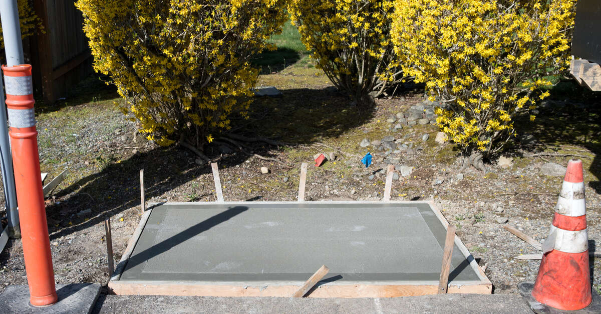 A cement pad poured with wood forms still in place, next to the road, for the installation of a new mailbox pedestal.