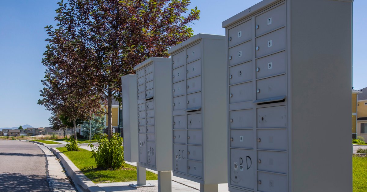 Cluster mailbox systems, with numbered individual mail slots, installed on a landscaped sidewalk in a neighborhood.