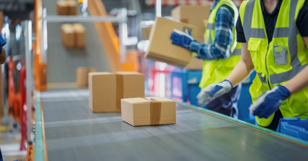People wearing PPE and working in a facility loading cardboard boxes onto an automated conveyor belt.