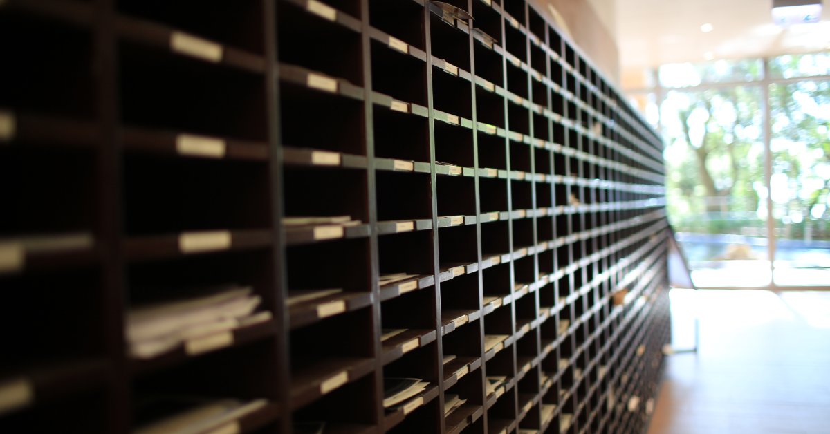 There are many rows and columns of cubby holes, some of the cubbies have mail in them. There is a window to the right.