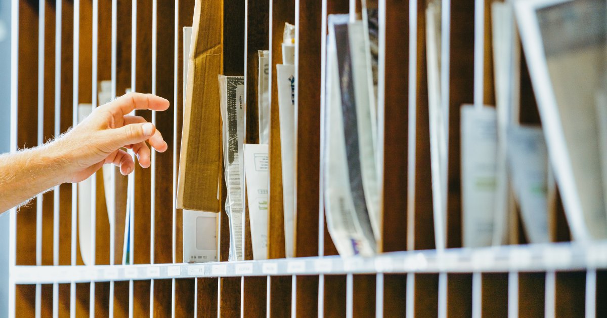 A hand is reaching into a cubby hole, the hole has several envelopes. There are multiple cubbies all in a row.