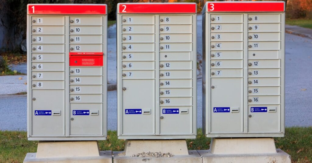 Several mailbox units in a row; there is a patch of grass behind them and a street behind the patch of grass.