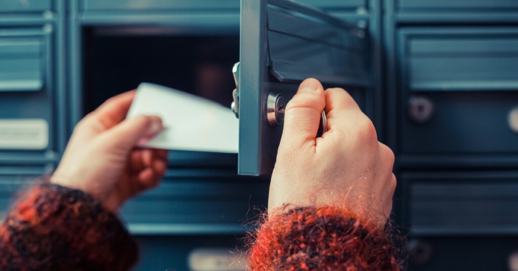 A person is opening a small mailbox. They are pulling out a slip of white paper. There are other mailboxes around the open one.