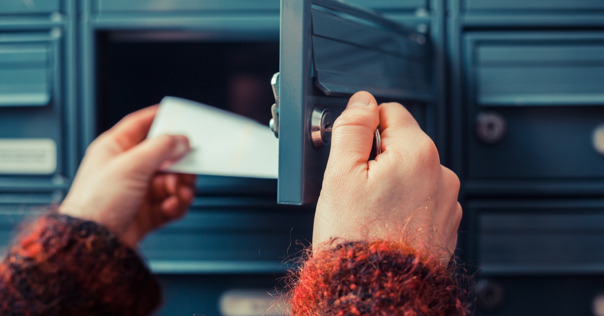 A person is opening a small mailbox. They are pulling out a slip of white paper. There are other mailboxes around the open one.