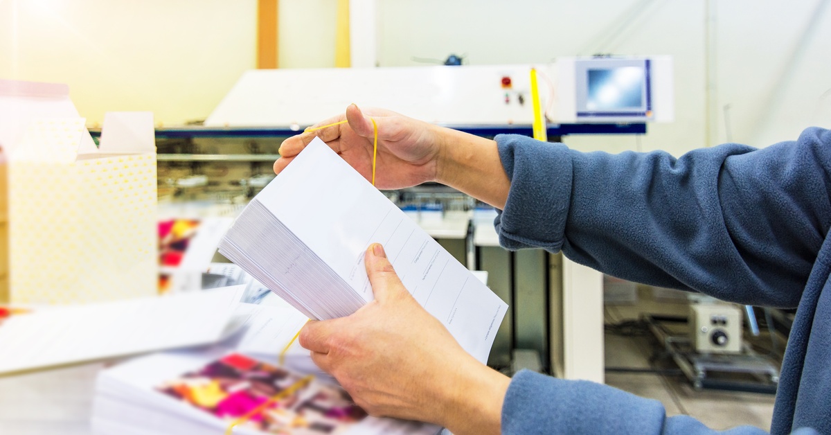 A person is holding a stack of envelopes. They are wrapping a rubber band around the stack.