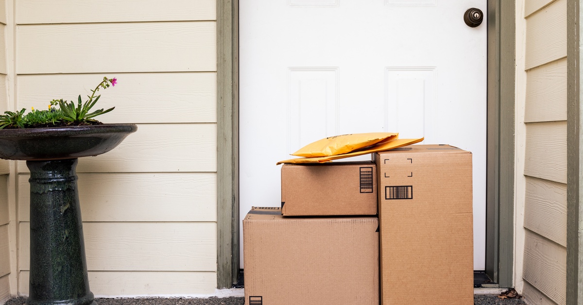A stack of boxes is sitting on a doorstep. There is a potted plant next to the stack of boxes.