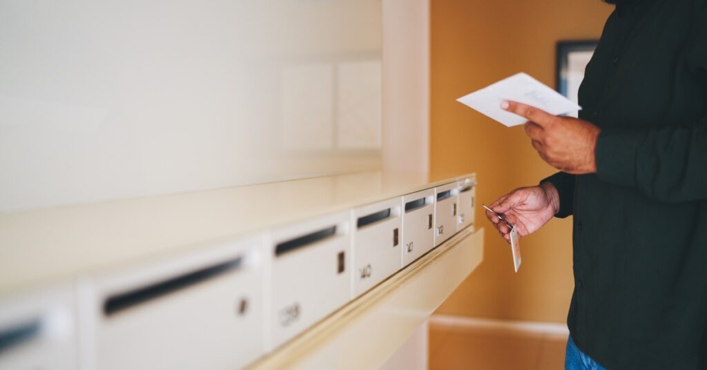 A man is holding a slip of paper as he stands in front of several mailboxes. He has a key in his other hand.