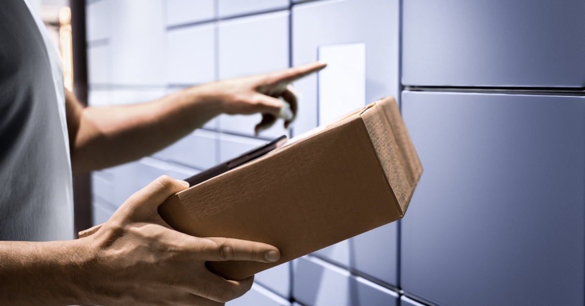 A person is holding a cardboard box in one hand and is pressing a touch screen with their other hand.