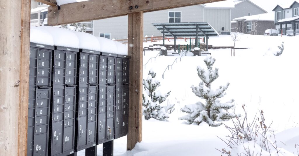 A cluster box unit out in the open. There is snow everywhere and there are houses in the background.
