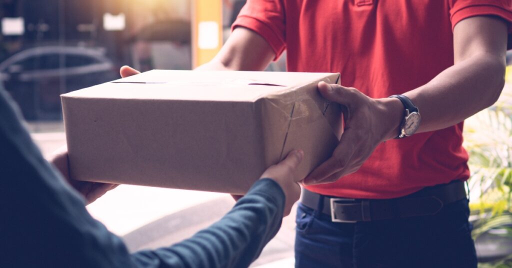 A man in a red shirt is handing a package to another person, who is reaching out and grabbing the package as well.