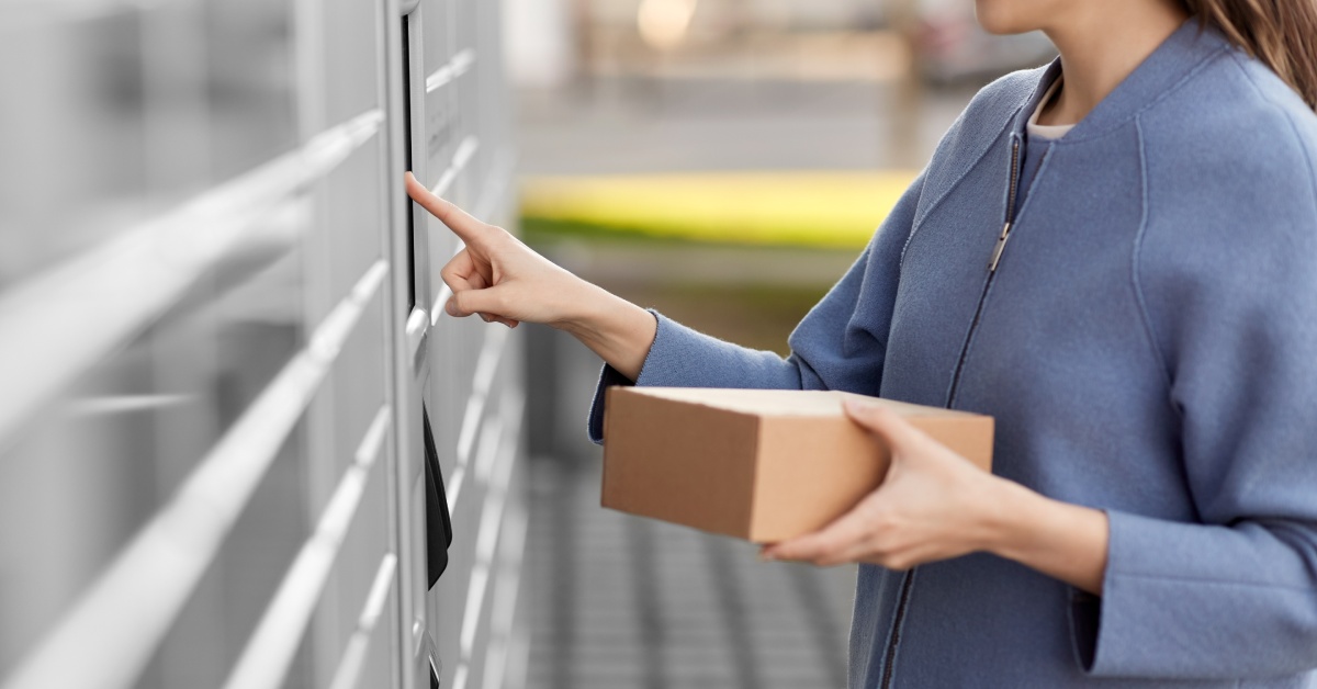 A smiling woman is holding a package in one hand and is using her other hand to press her finger against a surface.