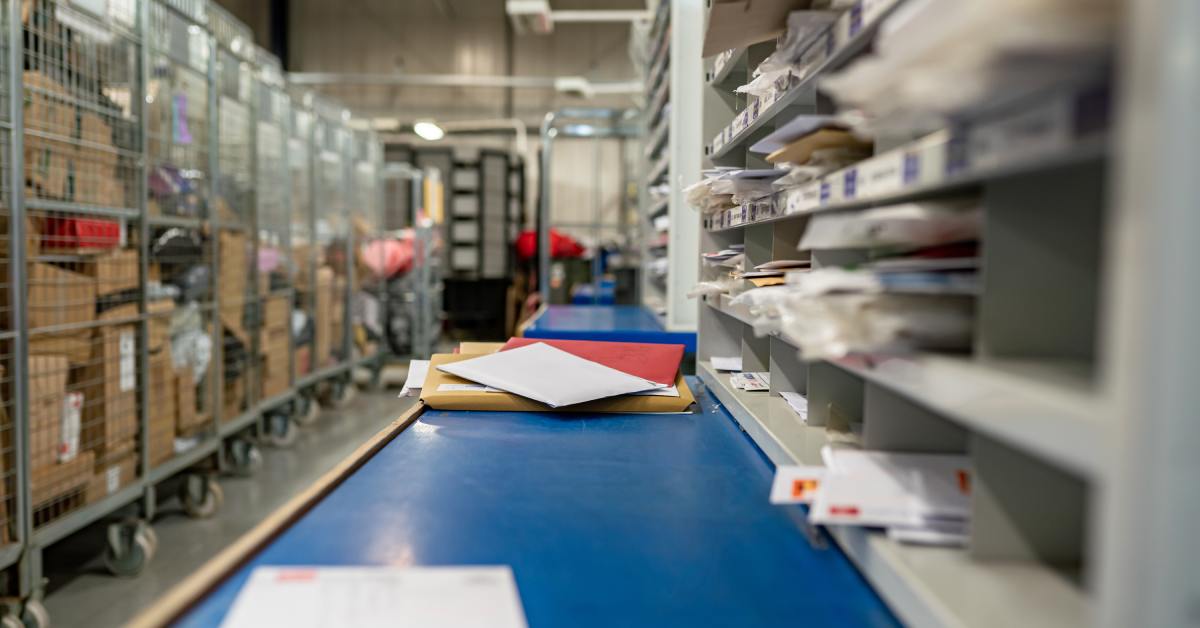 A large room with mail packaging strewn about. There are several envelopes on a blue tabletop.